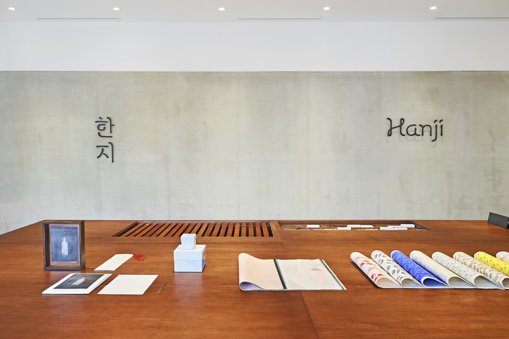 Hanji writing in Korean and Romanization on the back wall. Table with colorful Hanji paper layout on a table with other decorations