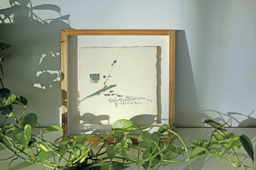 A framed painting on a hanji paper placed at the wall, decorated with green leaves infront