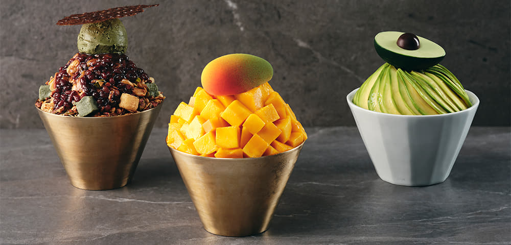 There are three bowls of Avocado Vegan Bingsu, mugwort bingsu, and mango bingsu, and there is a small bowl with toppings around it.