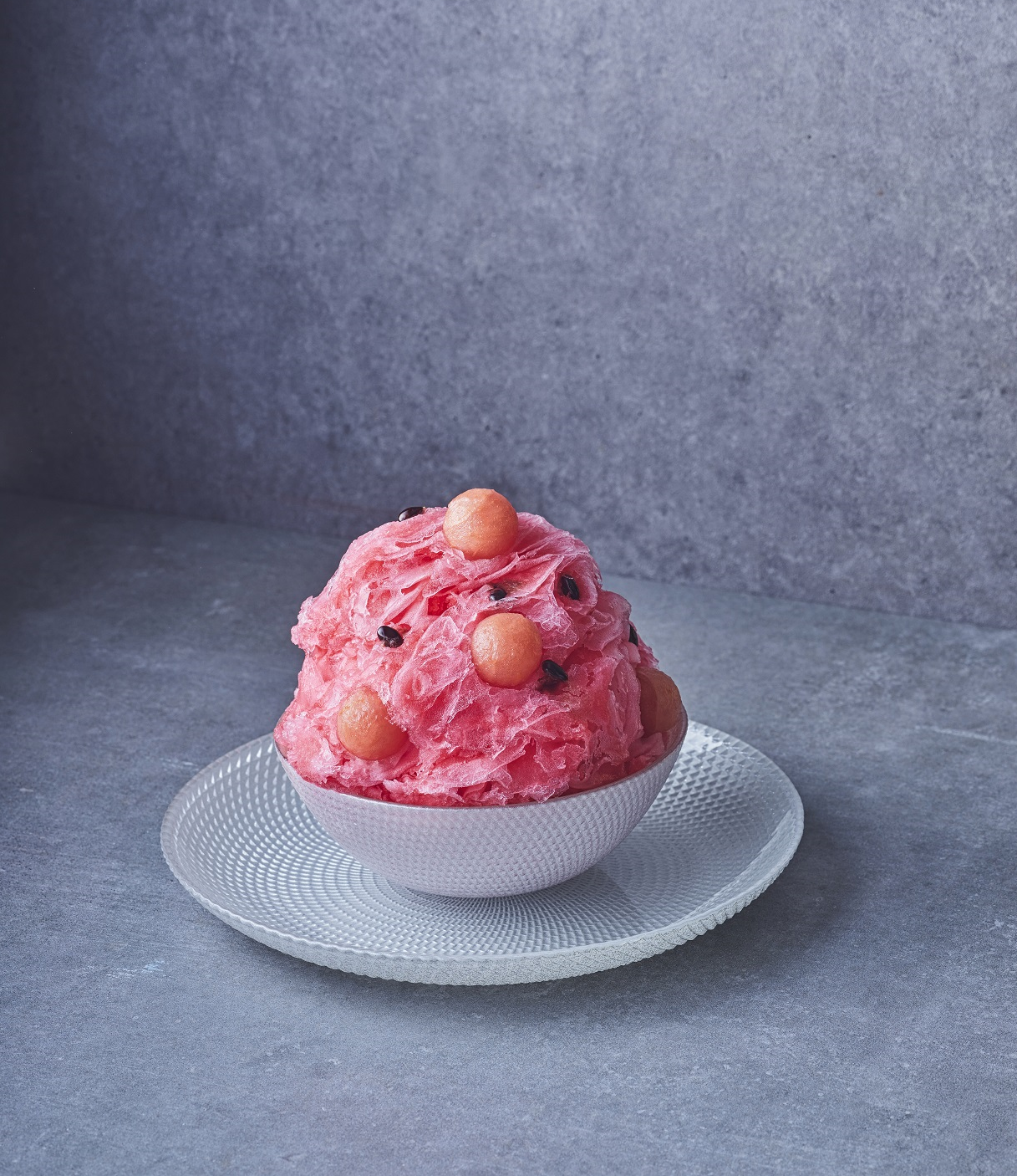 Red colored shaved ice with watermelon is placed on a plate.