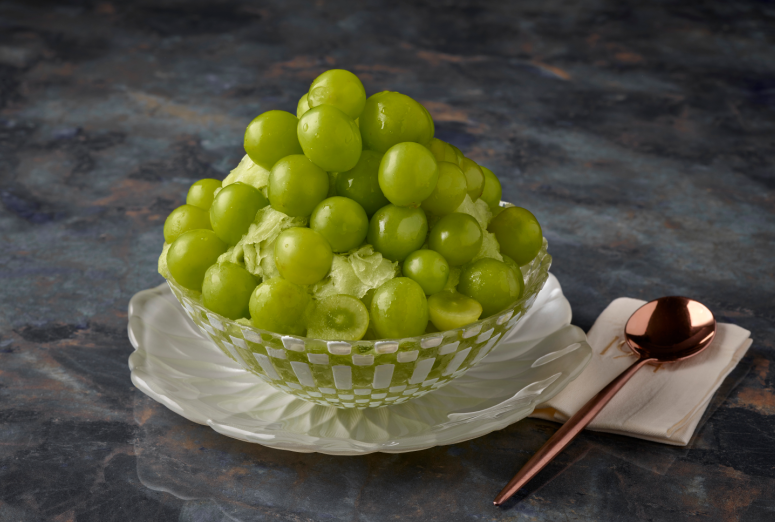 Shine Muscat Bingsu topped with Shine Muscats is placed in a glass bowl, and a spoon is placed next to it..