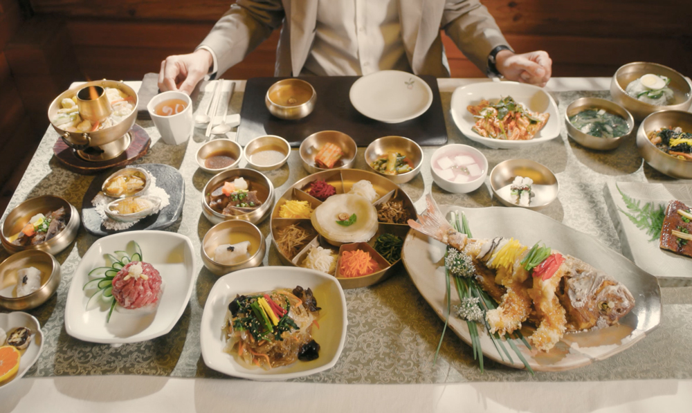 An image of a man sitting at a table that is filled with a variety of traditional Korean dishes