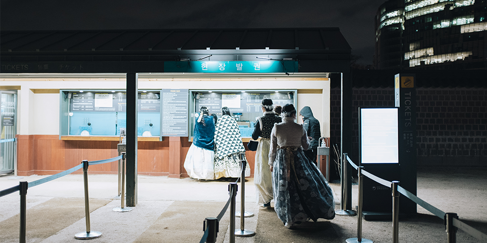 Pengunjung yang memakai hanbok sedang beratur di hadapan kaunter tiket.