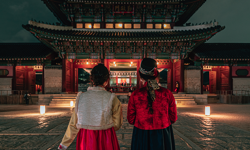 Dua wanita yang memakai hanbok sedang berjalan di hadapan Geunjeongmun Gate.