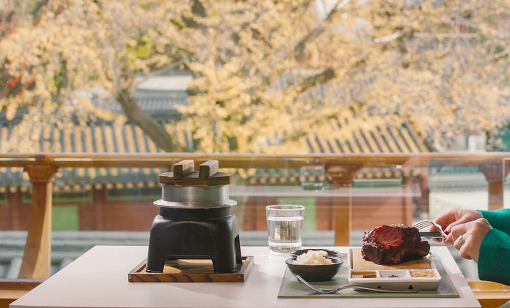 Foods delicately placed upon a table with a view of hanok in the background.